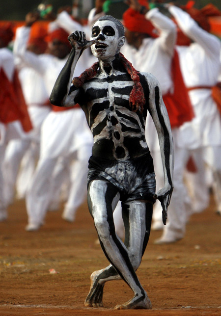 A man with a skeletal design painted on him gestures to show the ill effects of smoking and drinking.