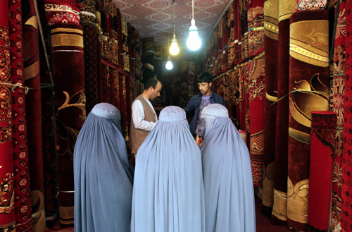 Afghan women talk to a carpet vendor in his shop in Kabul.