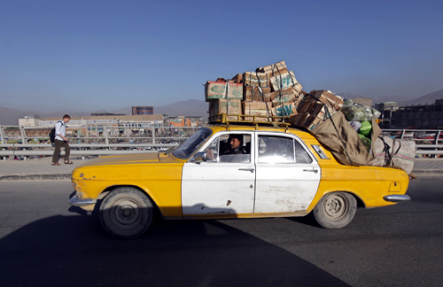 A Russian-made taxi loaded with boxes of vegetables and fruits drives down the road  in Kabul city.