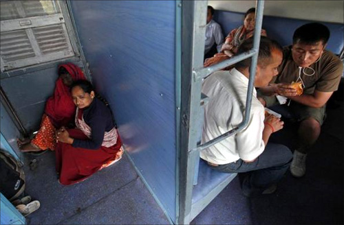 Women sit next to a door as men eat snacks inside the sleeper class compartment of the Kalka Mail passenger train.
