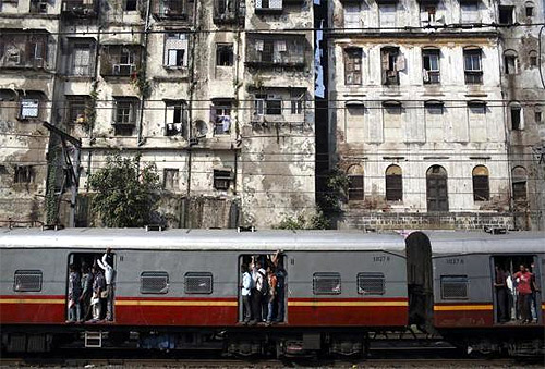 Commuters stand at the open doorways of a suburban train as they head toward their destination in Mumbai.
