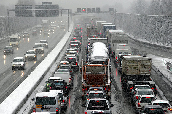Vehicles move slowly along a highway in a traffic jam during snowfall in Berlin.