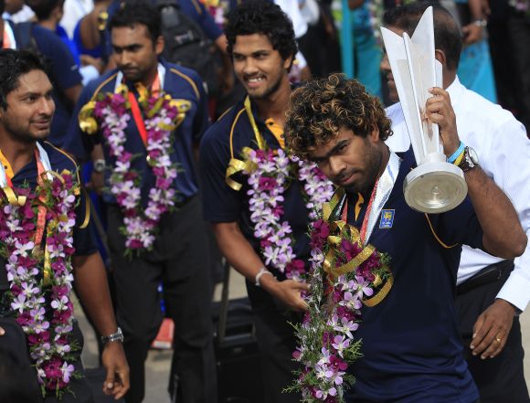 Sri Lanka's Twenty20 cricket team captain Lasith Malinga (right) displays the 2014 WT20 trophy to fans after arriving at the Bandaranaike International Airport