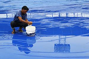 A man uses a sponge to soak up rain water collected on the ground covers in Margao on Friday