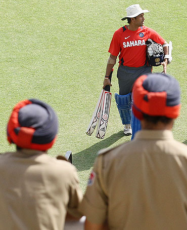 Sachin Tendulkar walks across the field while being watched by two policemen