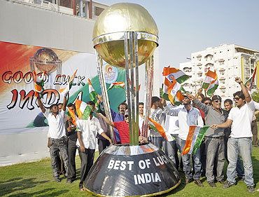 Car designer Sudhakar Yadav sits inside a three-wheeler car made in the shape of the Cricket World Cup trophy, in Hyderabad, as fans cheer, on the eve of the semi-final match between India and Pakistan
