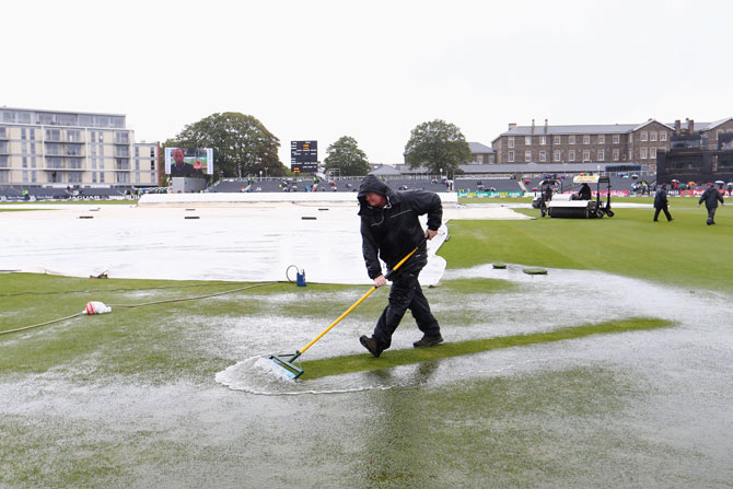 Groundstaff sweep away puddles from the outfield in vain as play is abandoned in the first ODI