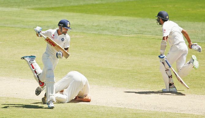 Virat Kohli and Murali Vijay run between the wickets as bowler Ryan Harris takes a tumble on the follow through to his run-up