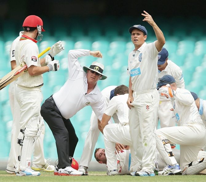 Phillip Hughes of South Australia is helped by New South Wales players after falling to the   ground after being struck in the head by a delivery