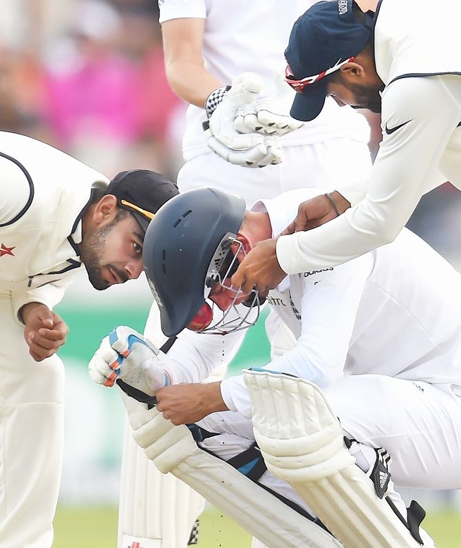 Indian fielders attend to England batsman Stuart Broad after he is hit by a ball through   the grill of his helmet