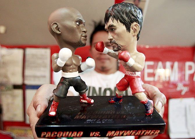 A store employee holds up a stand with miniature figurines of boxers Manny Pacquiao (right) of the Philippines and Floyd Mayweather Jr. of the U.S., at a mall in Manila