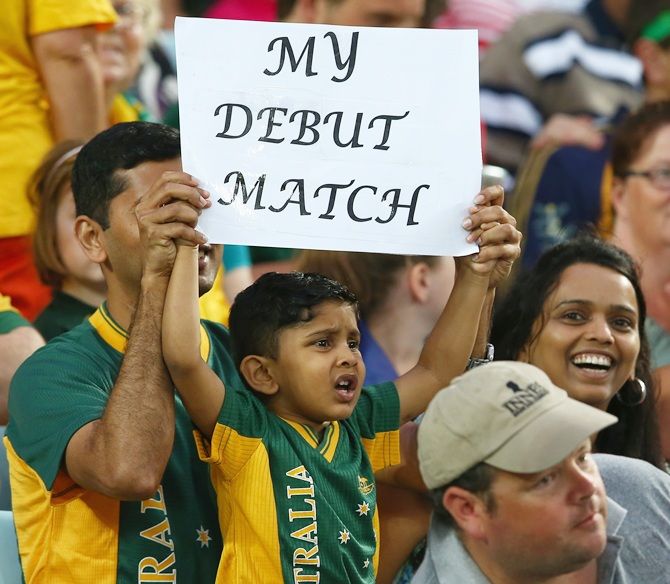 A young cricket fan in the crowd holds up a sign as he waits for the start of play