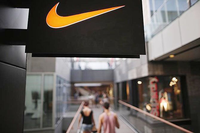 People walks past a Nike shop under the company logo at the Sanlitun shopping area in central Beijing