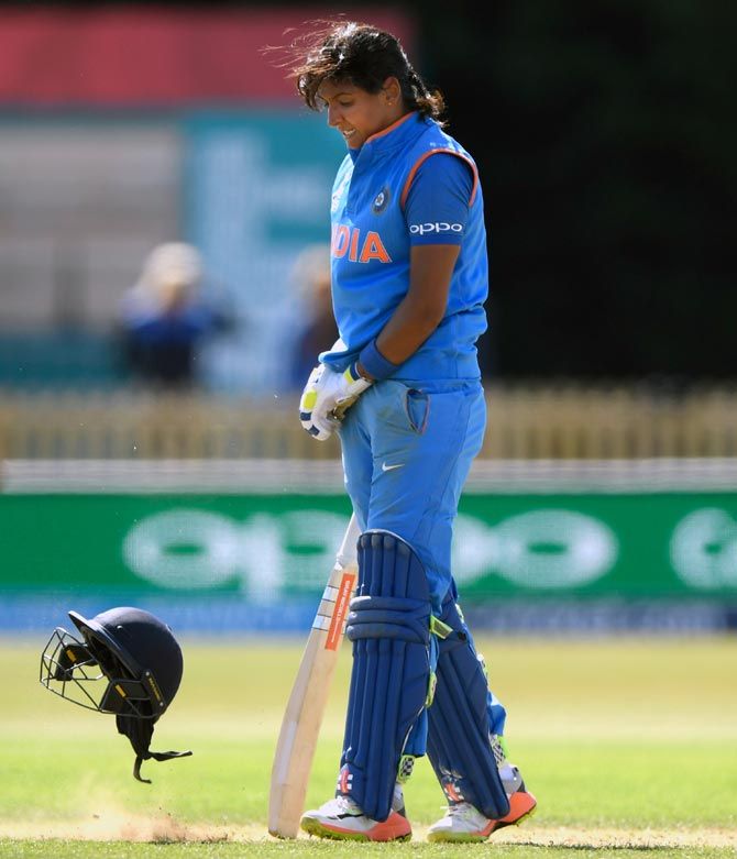 Harmanpreet Kaur reacts by throwing her helmet off onto the ground after reaching her century