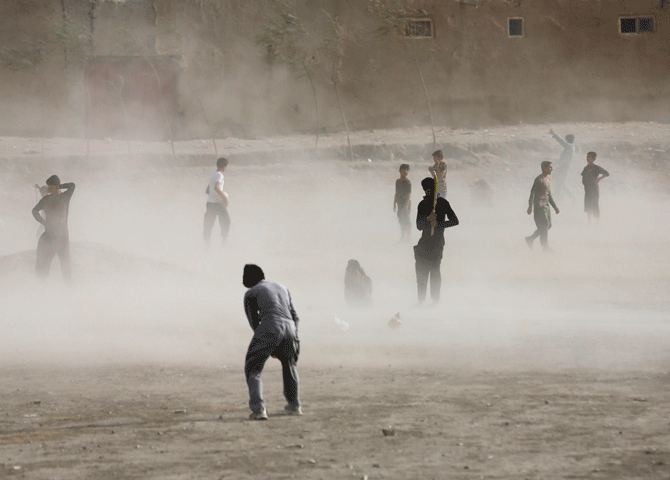 Afghan boy wait for a brief dust storm to pass while playing cricket in Kabul