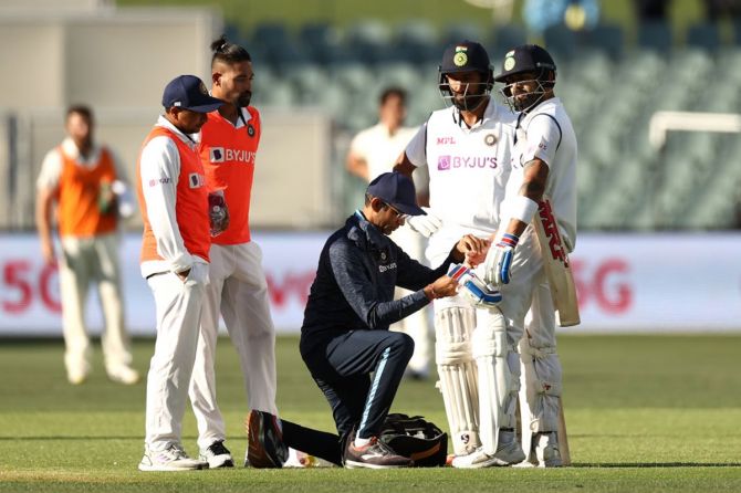 Cheteshwar Pujara watches as Virat Kohli receives medical attention after being hit in the hand by a delivery from Mitchell Starc.