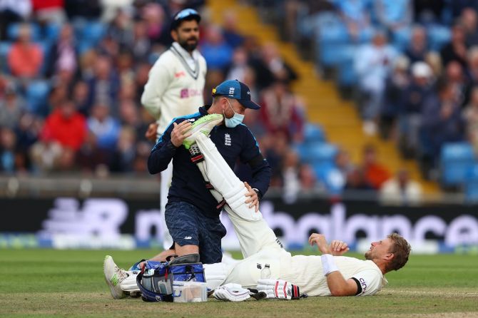 India captain Virat Kohli looks on as Joe Root receives treatment from a team physio for cramps.
