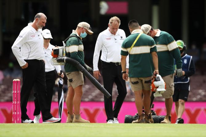 Umpire Paul Wilson, reserve umpire Claire Polosak and umpire Paul Reiffel watch as ground staff use blowers to dry a wet area after a rain delay on Day 1 of the third Test between Australia and India, at the Sydney Cricket Ground