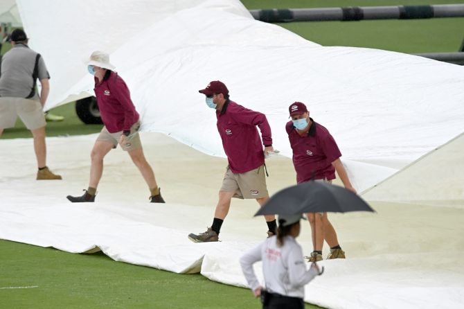 Groundsmen cover the pitch as rain halts play just before tea.