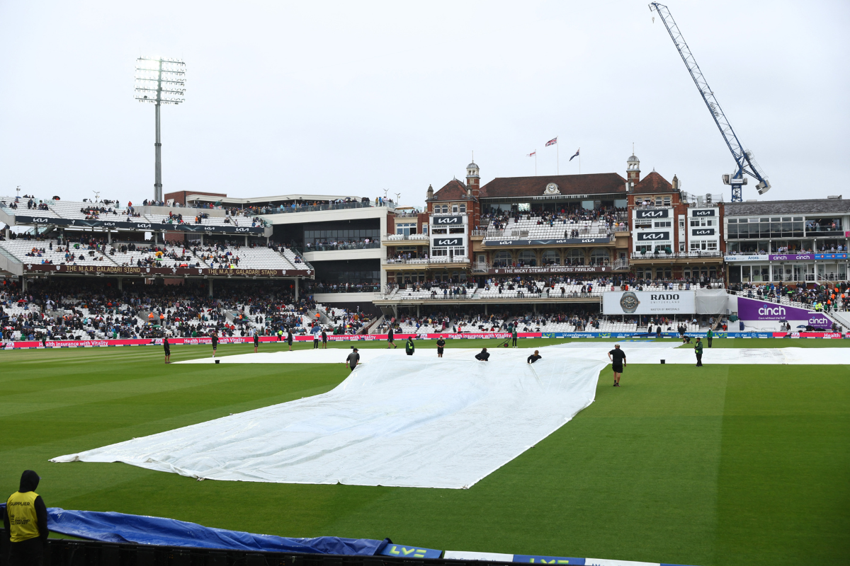 General view of covers being pulled over the wicket by groundstaff as rain stops play
