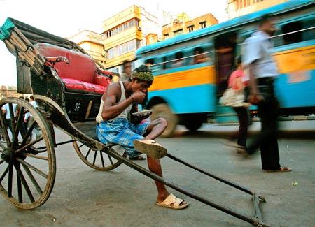 A rickshaw puller eats beside a busy road in Kolkata.