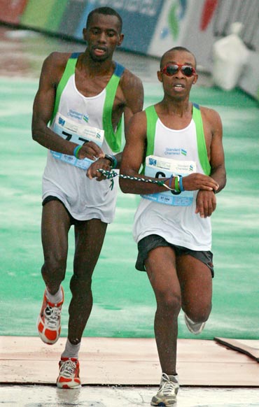 Kenyan blind runner Henry Wanyoike Wahu (R) and his guide Joseph Kibunja mark their time while crossing the finish line during the Hong Kong Marathon