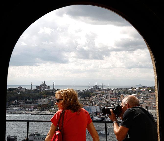 Tourists, with the Hagia Sophia museum (L) and Blue Mosque (R) in the background, look at the old city from the historical Galata Tower in Istanbul