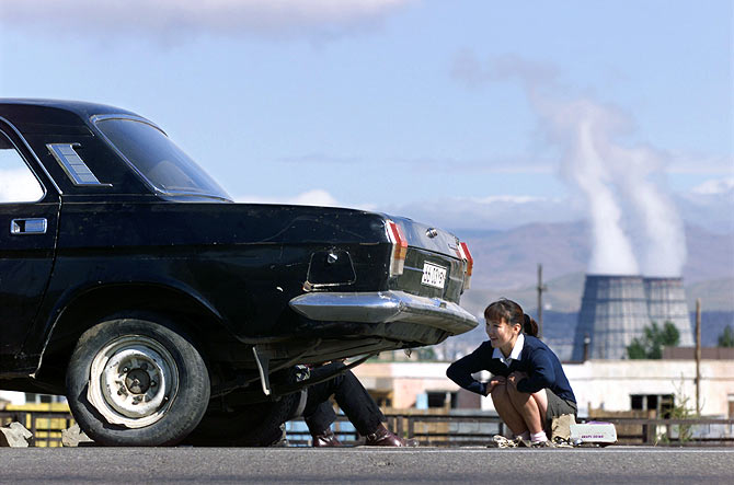 A Mongolian woman squats next to her broken down car near a power plant in Ulan Bator