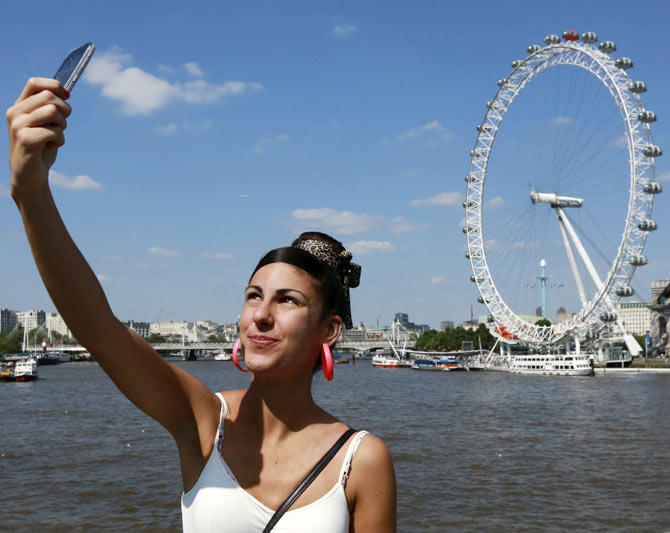 A tourist takes a picture of herself in front of the River Thames and the London Eye in central London.