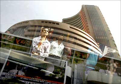 The Bombay Stock Exchange building is reflected on a glass window as people look at a large screen displaying the benchmark share index.