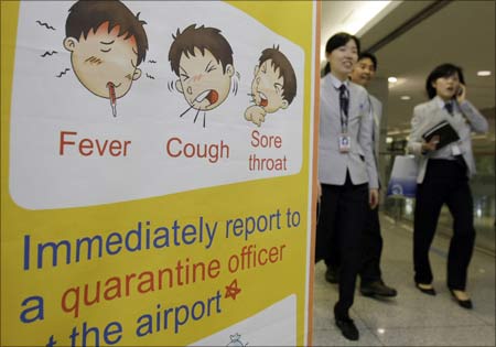 An airport worker monitoring passengers for signs of fever walks past a health poster at Taoyuan International Airport, northern Taiwan. | Photograph: Nicky Loh/Reuters
