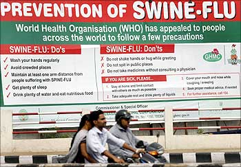 People ride past a billboard carrying messages on prevention of the swine flu.