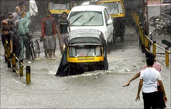People and vehicles move through a flooded road during heavy rainfall in Mumbai on July 14, 2009.