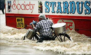 A man pushes a bicycle as a bus passes by along a flooded road after heavy rainfall in Mumbai.