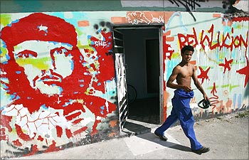 A man walks out of a building adorned with a portrait of Che Guevara and the word 'revolution' in Old Havana.