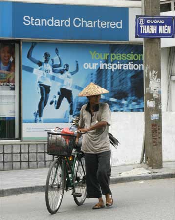 A man pushes a bicycle past an ATM booth of the Standard Chartered Bank in Hanoi.