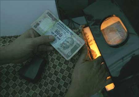 A man uses an electronic machine to check a hundred rupee note.