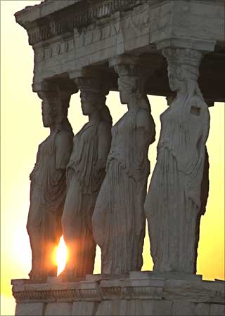 The sun sets behind the temple Erechtheion's Porch of Maidens at the Acropolis in Athens, Greece.