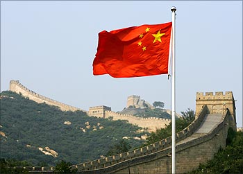 A Chinese flag flies in front of the Great Wall of China.
