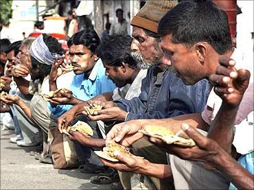 Poor people eat food in front of a temple in New Delhi.