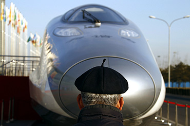 A man wearing a traditional Chinese hat looks at a high-speed train.
