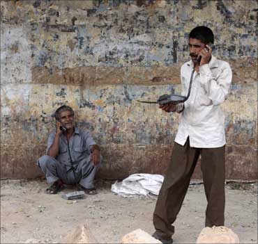 Two men speak on telephones at a roadside telephone booth in New Delhi.