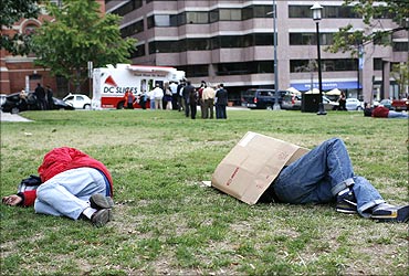 Homeless men sleep in a park while people wait in line to purchase pizza in Washington.
