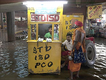 People sit in a flooded phone booth at a bus station after heavy rains in New Delhi.