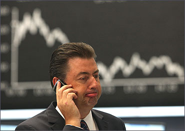 A man uses his cell phone in front of a graph showing the day's performance of the DAX index at the Frankfurt Stock Exchange.