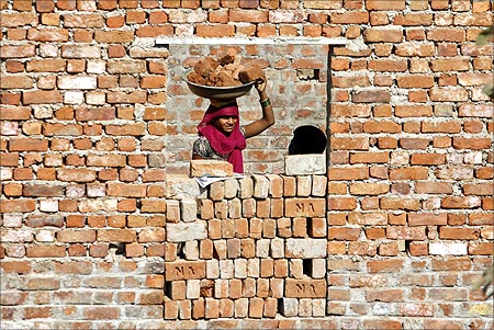A construction labourer carries bricks on her head at the construction site of a residential estate.
