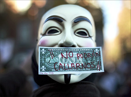A protester wearing a Guy Fawkes mask, symbolic of the hacktivist group Anonymous, is pictured with a fake dollar bill.