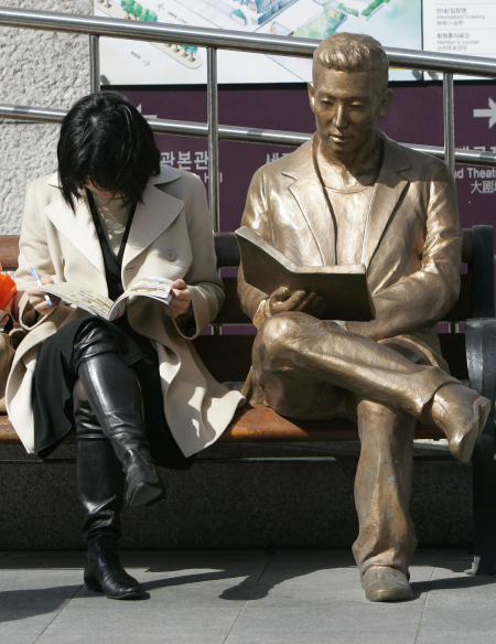 A woman reads a book beside a bronze statue in front of Sejong Centre for the Performing Arts in central Seoul.