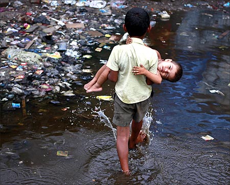 Ashfaq, 10, carries his two-year-old brother Farhaan through a flooded pathway in a Mumbai slum.
