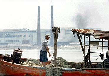 A Chinese fisherman works on the Pearl River against a backdrop of a factory in Zengcheng, Guangdong